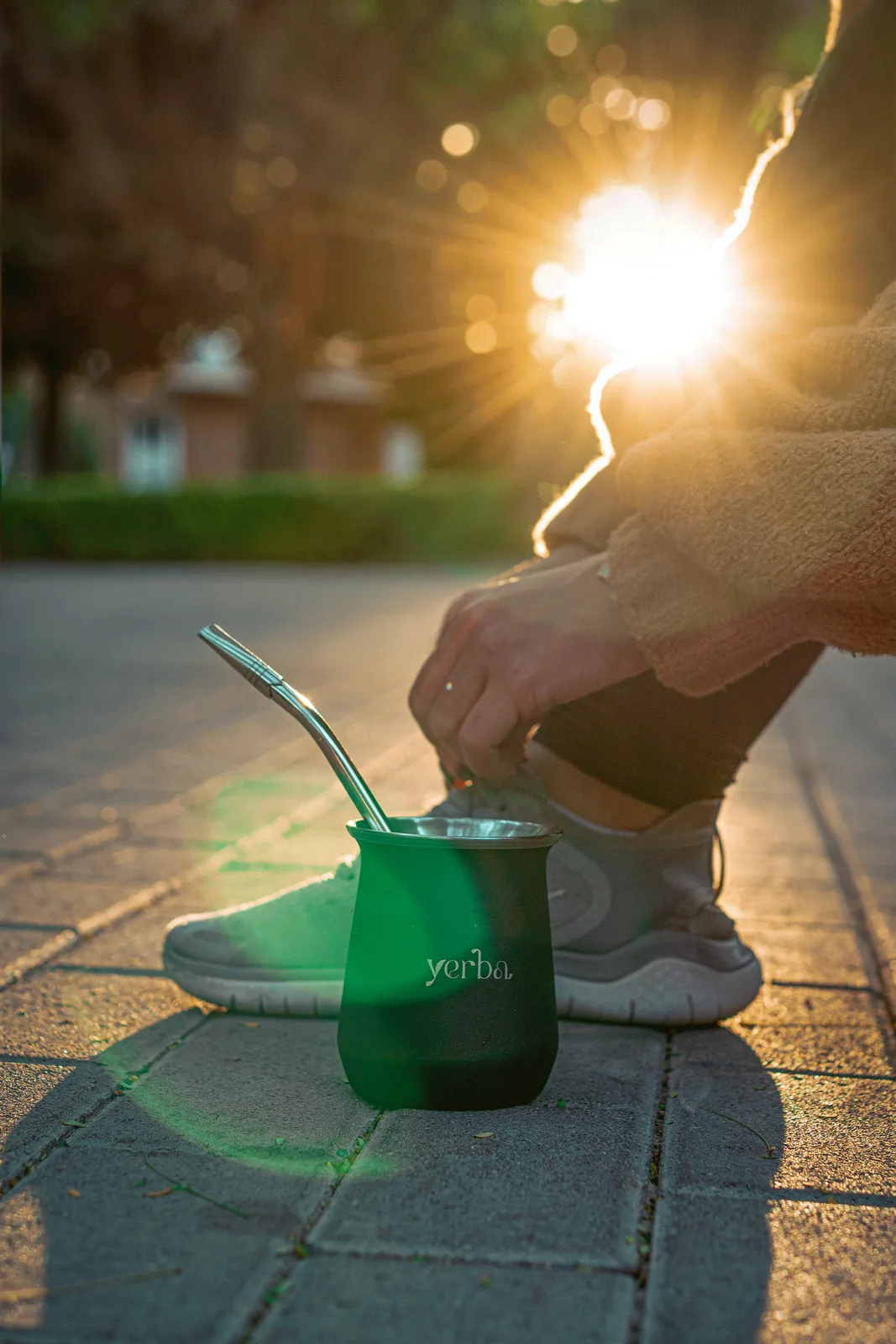 A green Yerba gourd and bombilla on a pavement in late afternoon light