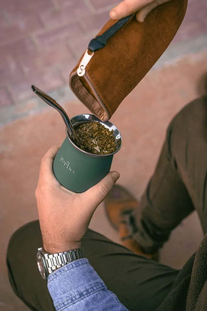 Hand pouring loose mate leaf from a leather pouch into a green gourd